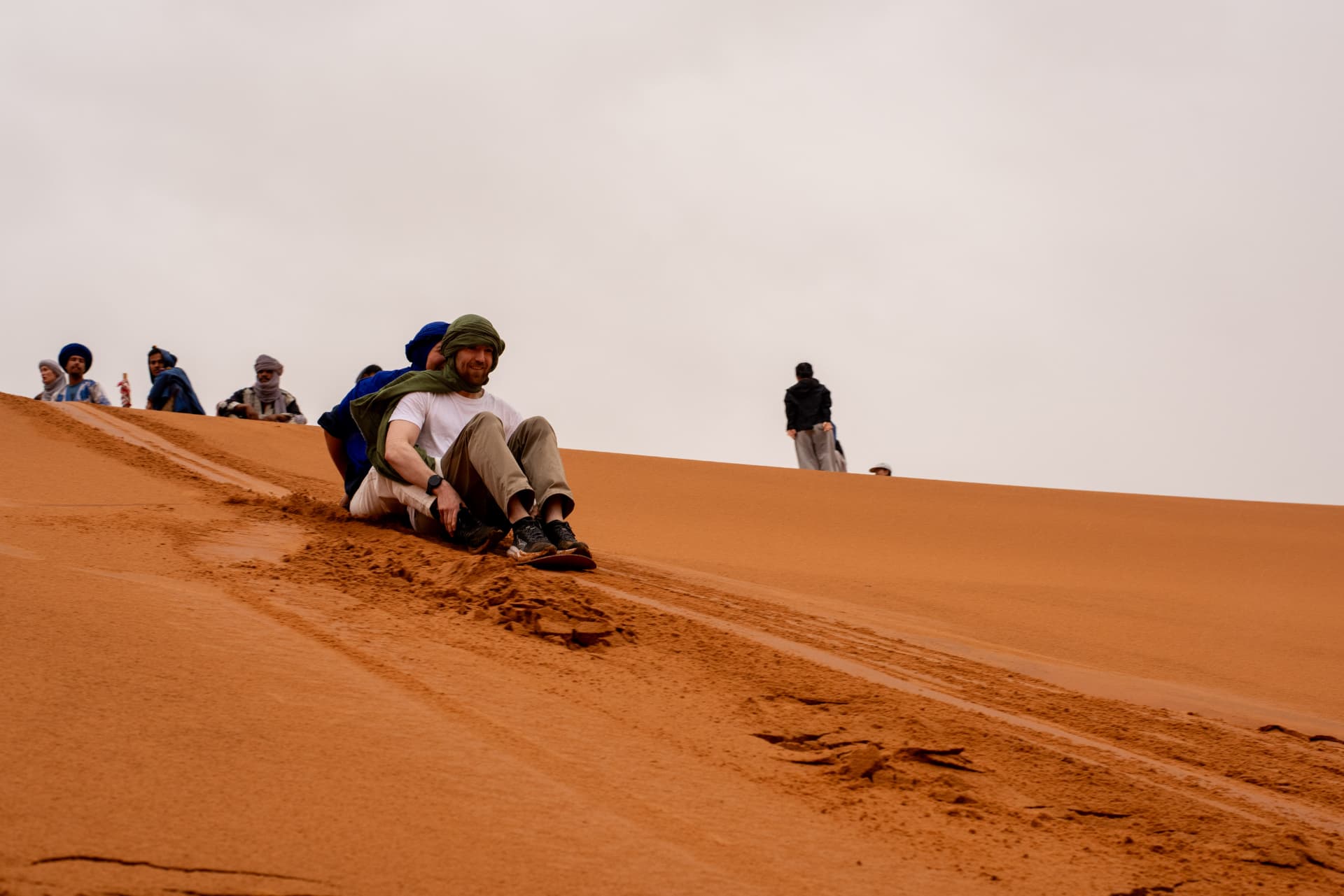 Traveller sliding down a golden sand dune in the Sahara Desert