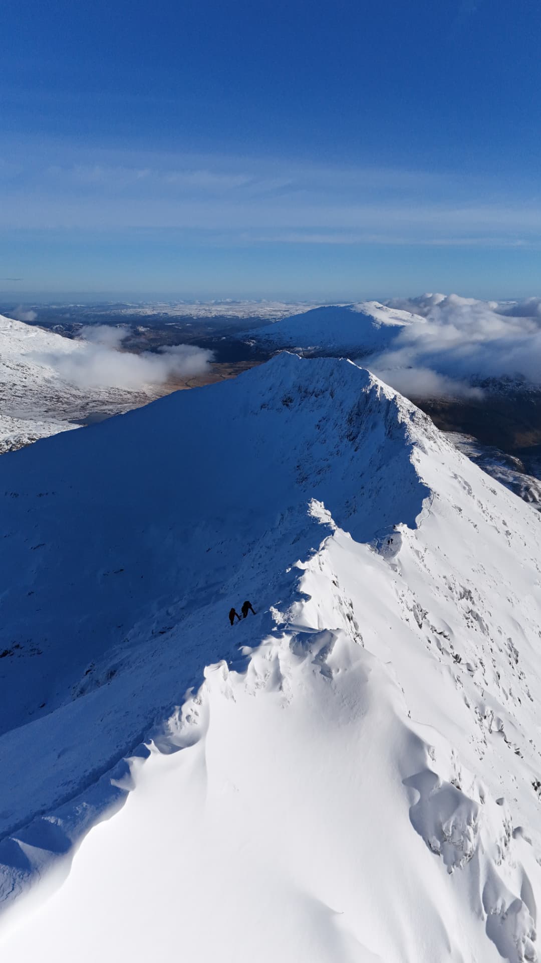 Snow-covered mountain ridge with two walkers under a clear blue sky