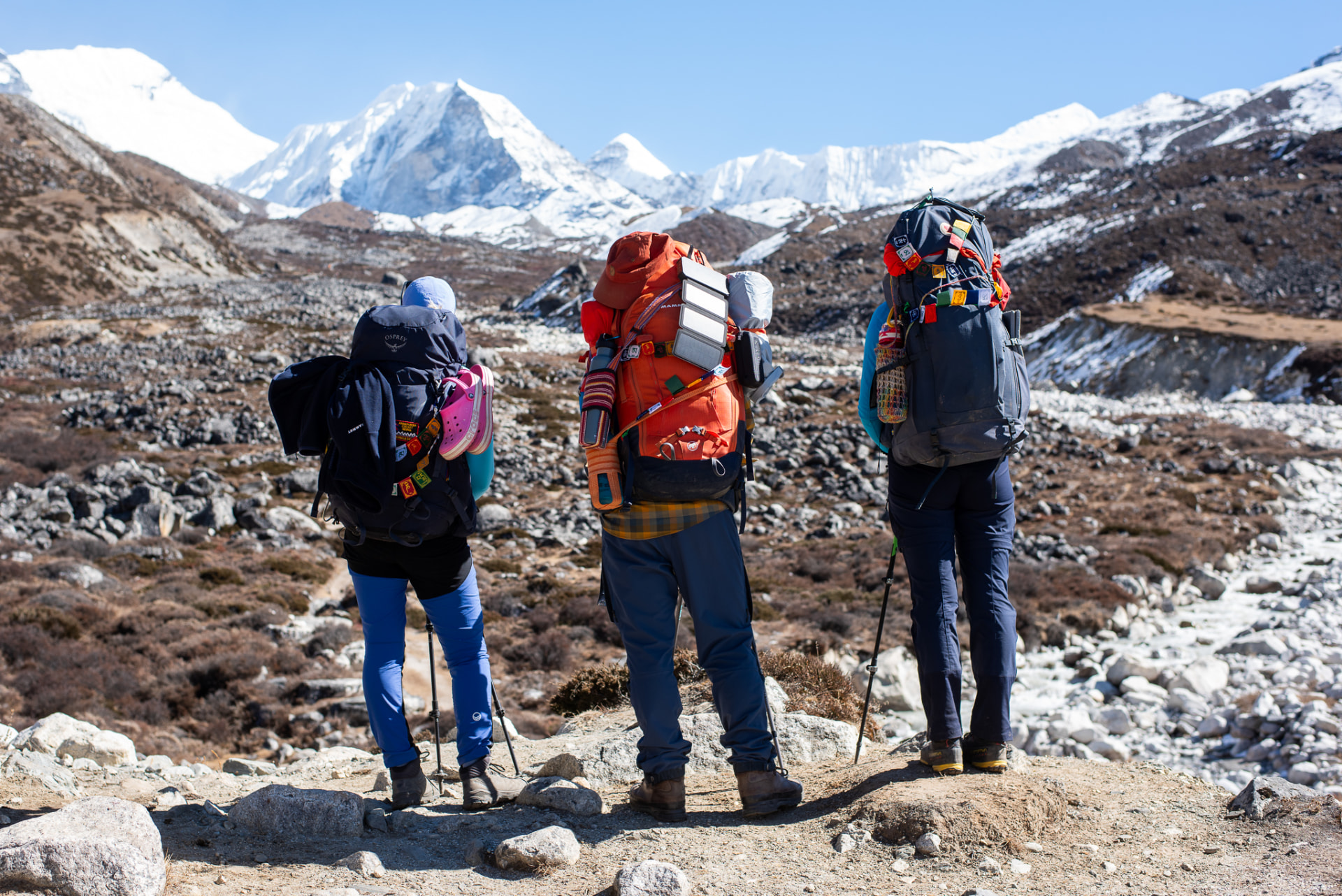Three trekkers with large packs looking toward snow-capped Himalayan peaks