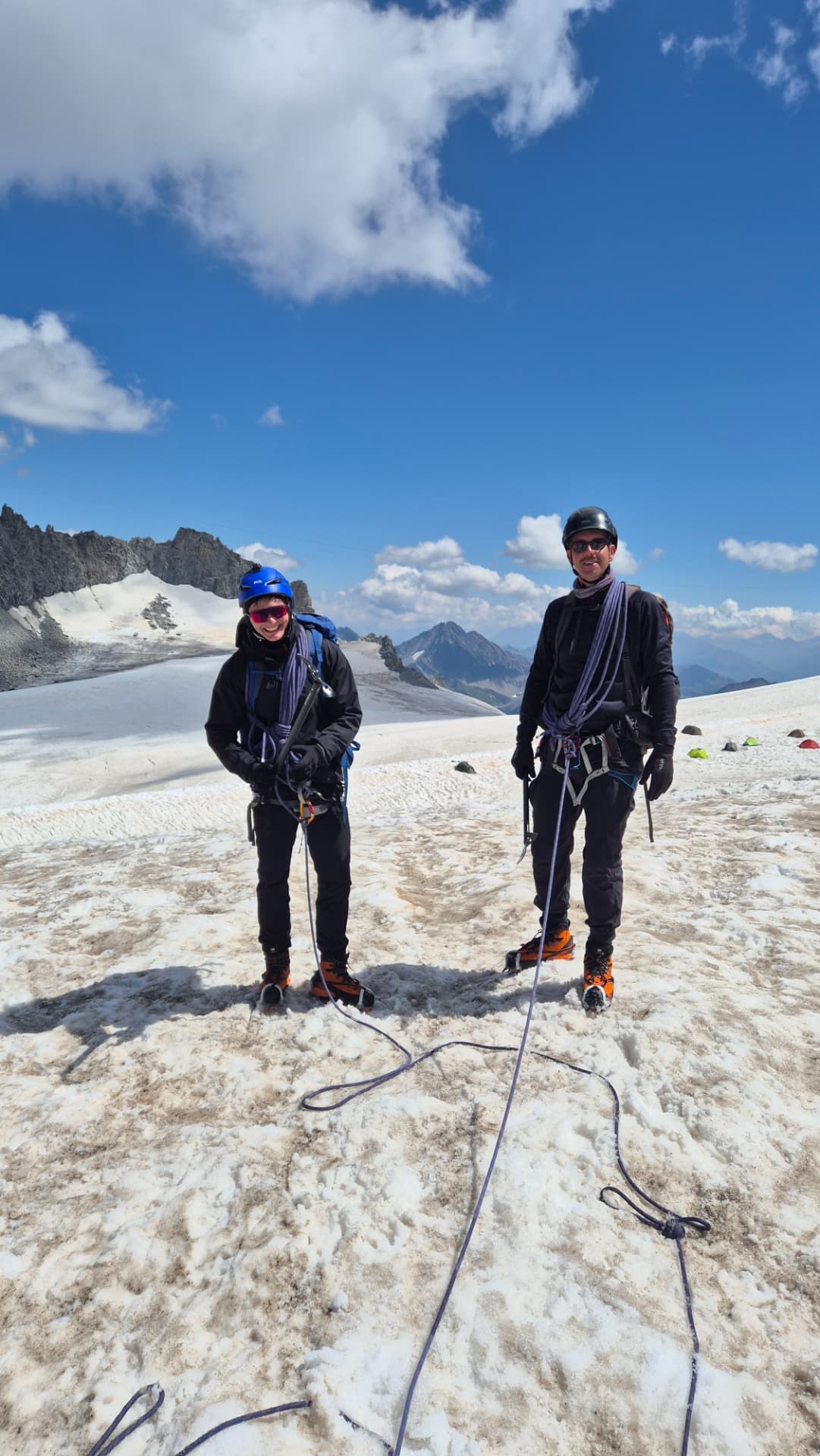 Two climbers roped together on a snowy Alpine glacier beneath a bright blue sky